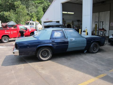 1991 Ford LTD Crown Victoria - A Ford Crown Victoria is being worked on, with parts of it taped off for painting. Other vehicles are visible in the background.