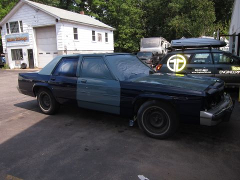 1991 Ford LTD Crown Victoria - A two-tone sedan is parked outside a garage, with another vehicle and a trailer behind it.