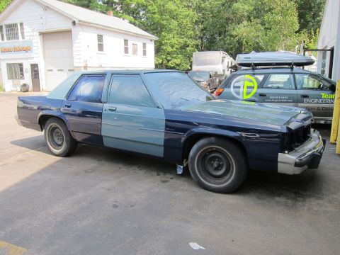 1991 Ford LTD Crown Victoria - A 1991 Ford Crown Victoria LTD is seen from the front-three-quarter angle, partially covered in masking for a paint job.
