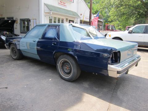 1991 Ford LTD Crown Victoria - A Ford Crown Victoria is parked outside a body shop, showing two-tone paint and protective tape on the windows.