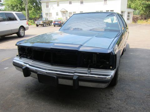 1991 Ford LTD Crown Victoria - A dark blue sedan is parked outside, missing its headlights and grille, with a prominent chrome bumper.