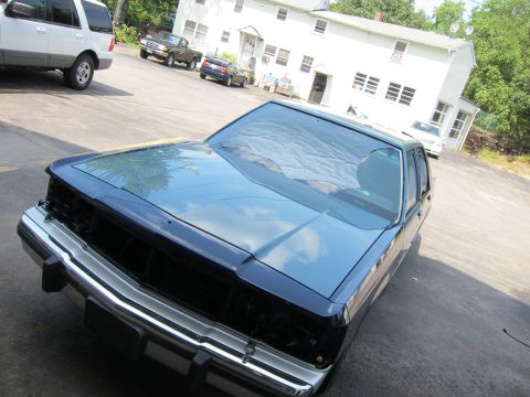 1991 Ford LTD Crown Victoria - Front view of a dark-colored 1980s Ford sedan with a missing grille, parked outside.
