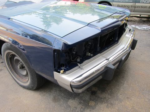 1991 Ford LTD Crown Victoria - The front of a blue car shows damage and missing parts, suggesting it is undergoing repairs or has been neglected.