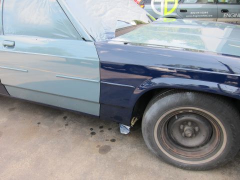 1991 Ford LTD Crown Victoria - A car with a blue fender and a gray door, partially covered with plastic, sits on a concrete surface with oil stains.