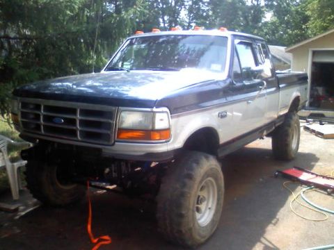 1993 Ford F-150 - This two-tone pickup truck features a lifted suspension and oversized tires, suggesting off-road modifications.
