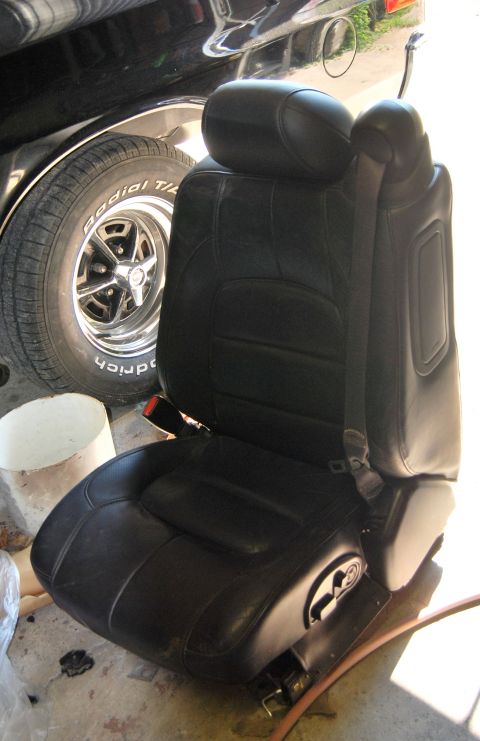 1975 Ford Ranchero - A black leather car seat is shown next to a car's tire and wheel.