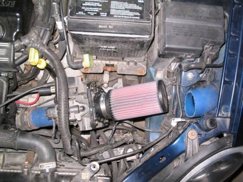 2000 Dodge Neon - Engine bay of a blue vehicle shows an aftermarket K&N air filter and associated intake plumbing.