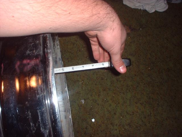 Tape measure held across a chrome wheel to measure backspacing on a shop floor