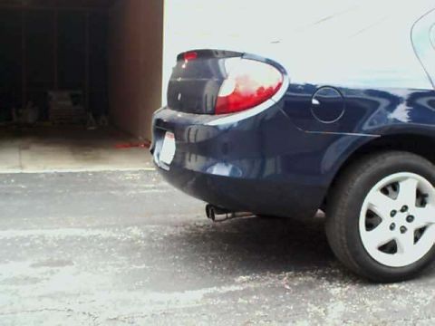 2000 Dodge Neon - The rear quarter panel and taillight of a dark blue sedan are visible, parked near a garage.