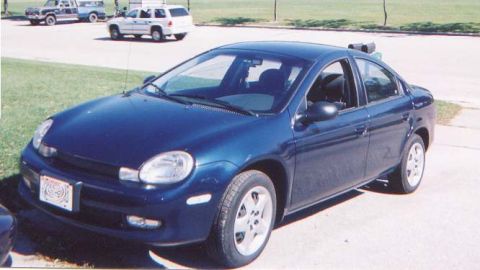 2000 Dodge Neon - A blue 2000 Dodge Neon sedan is parked on a paved surface with grass and other vehicles nearby.