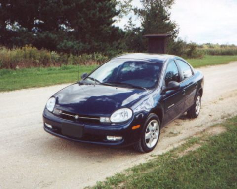 2000 Dodge Neon - A dark blue sedan is parked on a dirt road with trees and grass in the background.