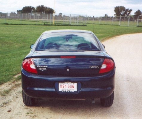 2000 Dodge Neon - The rear of a Dodge Neon is parked on a dirt road next to a grassy field.