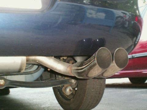 2000 Dodge Neon - Close-up view of the dual exhaust pipes on the rear of a dark blue vehicle, with another car partially visible.