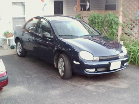 2000 Dodge Neon - A dark blue 2000 Dodge Neon sedan is parked on an asphalt driveway next to a house.