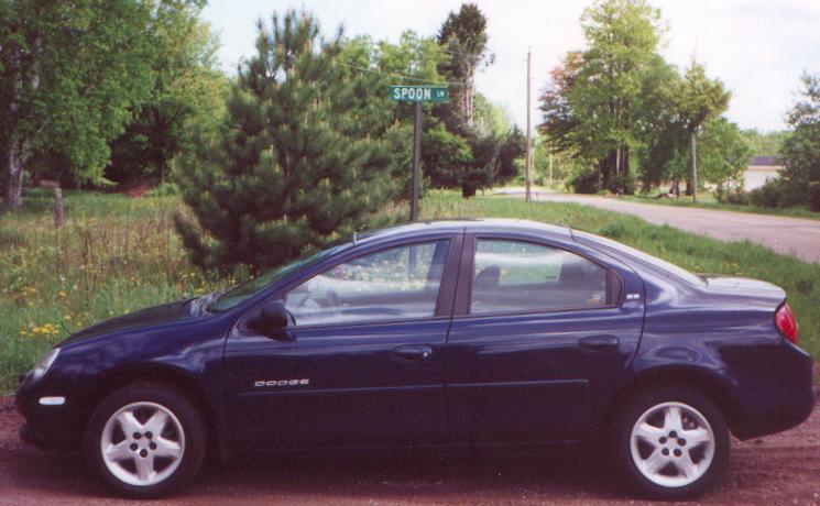 Dark blue 2000 Dodge Neon sedan parked on dirt road next to a grassy area with trees