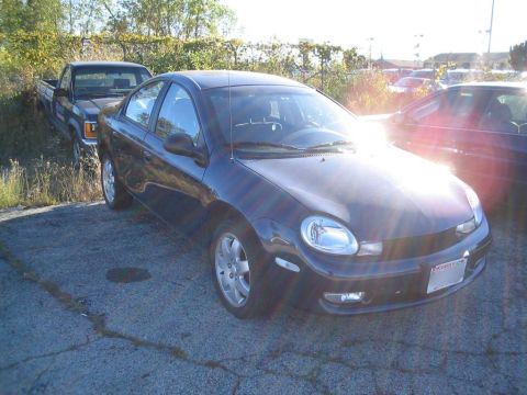 2000 Dodge Neon - A dark sedan is parked in a lot next to a pickup truck, with the sun shining brightly.