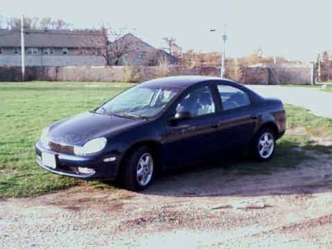 2000 Dodge Neon - A dark blue 2000 Dodge Neon sedan is parked on a gravel lot next to a grassy area.
