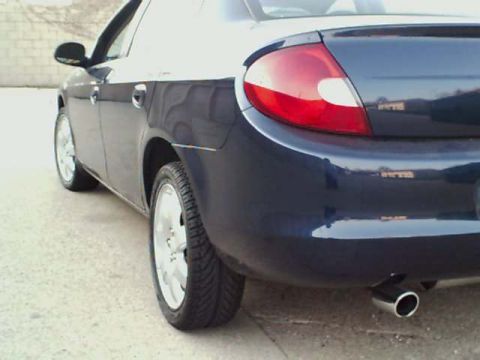 2000 Dodge Neon - The rear of a dark blue sedan is visible, with a chrome exhaust tip and a partial view of the taillight.