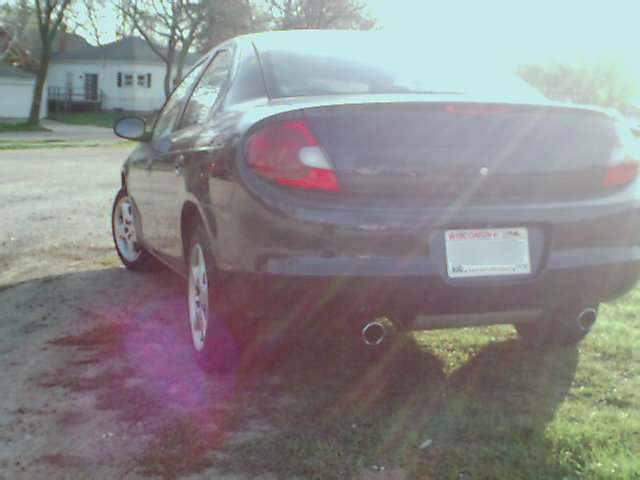 Dark sedan, 2000 Dodge Neon, rear view, parked on grass and dirt