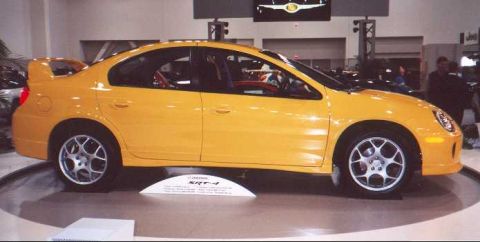 2000 Dodge Neon - A yellow sedan with a prominent rear spoiler is displayed on a turntable.