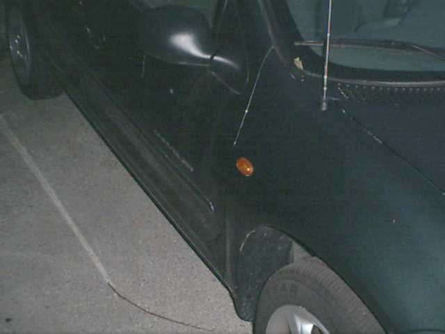 Side view of a dark car, showing fender, door, and side mirror. Orange turn signal visible on fender