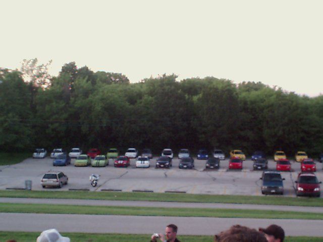 Many cars parked in a lot with trees in the background