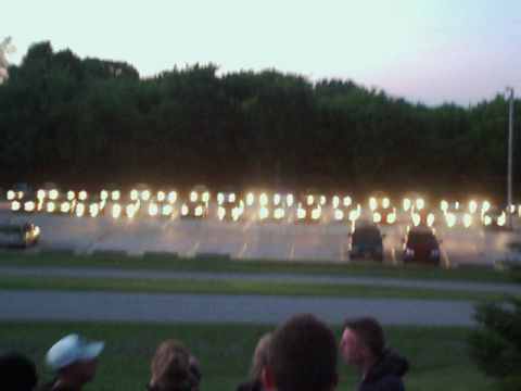2000 Dodge Neon - A long line of vehicles are parked with their headlights illuminated in a lot at dusk.