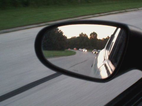 2000 Dodge Neon - A view of traffic ahead seen in a side mirror as the sun sets, with several vehicles on a winding road.