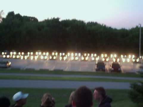 2000 Dodge Neon - A long line of cars with their headlights illuminated in a parking lot as dusk settles.