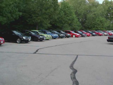 2000 Dodge Neon - A variety of sedans are parked in a lot, with trees forming a backdrop.