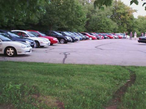 2000 Dodge Neon - A row of cars, including a white 2000 Dodge Neon, are parked in a lot with trees in the background.