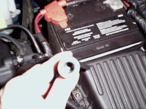 2000 Dodge Neon - Close-up of a hand holding a spark plug near a car battery and air intake system.