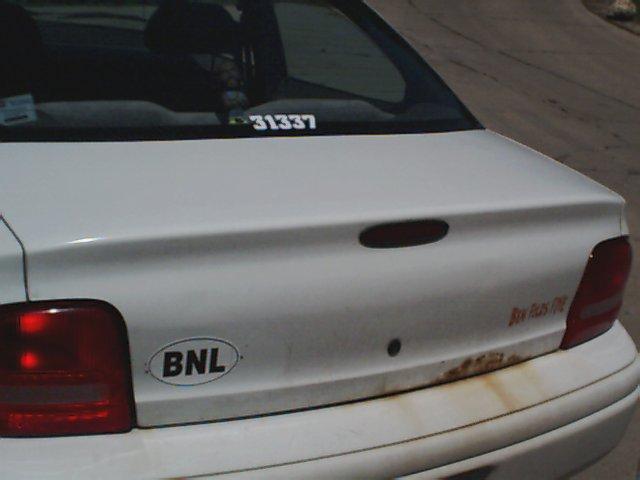 Rear of a white sedan showing taillight, trunk lid with a BNL sticker and a number sticker