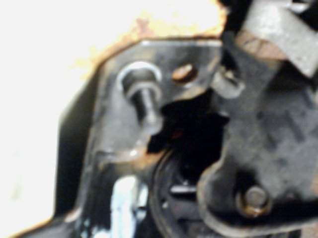 Close-up of a rusty metal bracket with a bolt, part of a vehicle's suspension