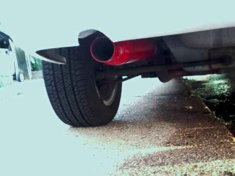 1995 Plymouth Neon - A bright red exhaust pipe is visible near the rear tire of a white vehicle.