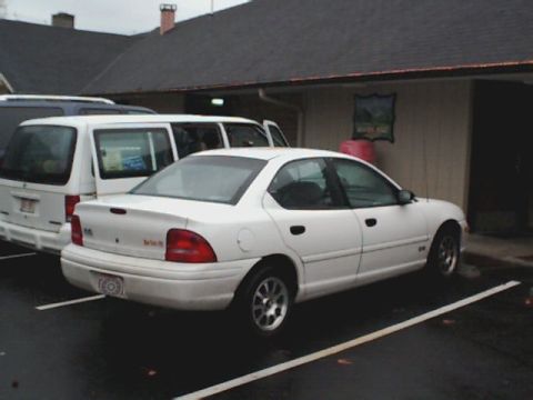 1995 Plymouth Neon - A white 1995 Plymouth Neon sedan is parked in a lot next to a white van.