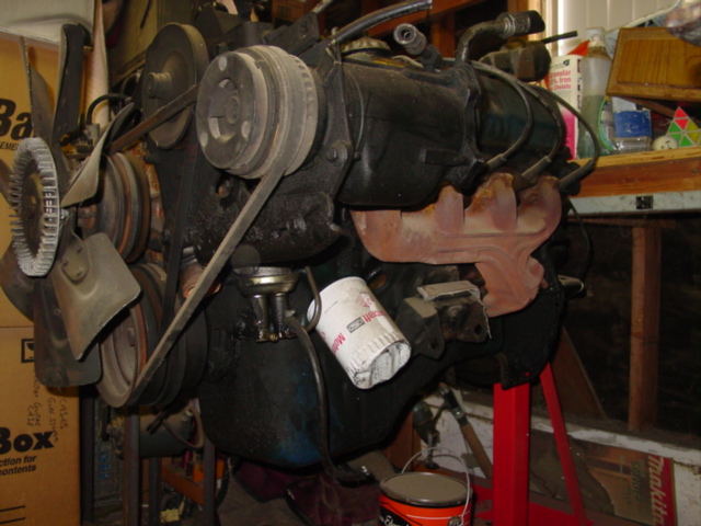 Bare V8 engine on a red engine stand in a garage, exhaust manifold visible