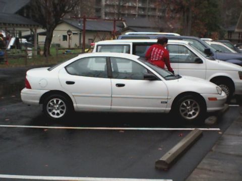 1995 Plymouth Neon - A white 1995 Plymouth Neon sedan is parked in a lot next to other vehicles.