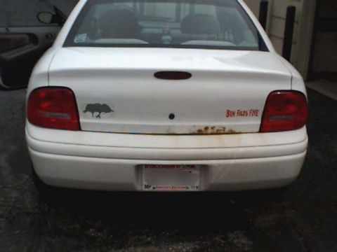 1995 Plymouth Neon - Rear view of a white sedan showing bumper stickers and rust damage.