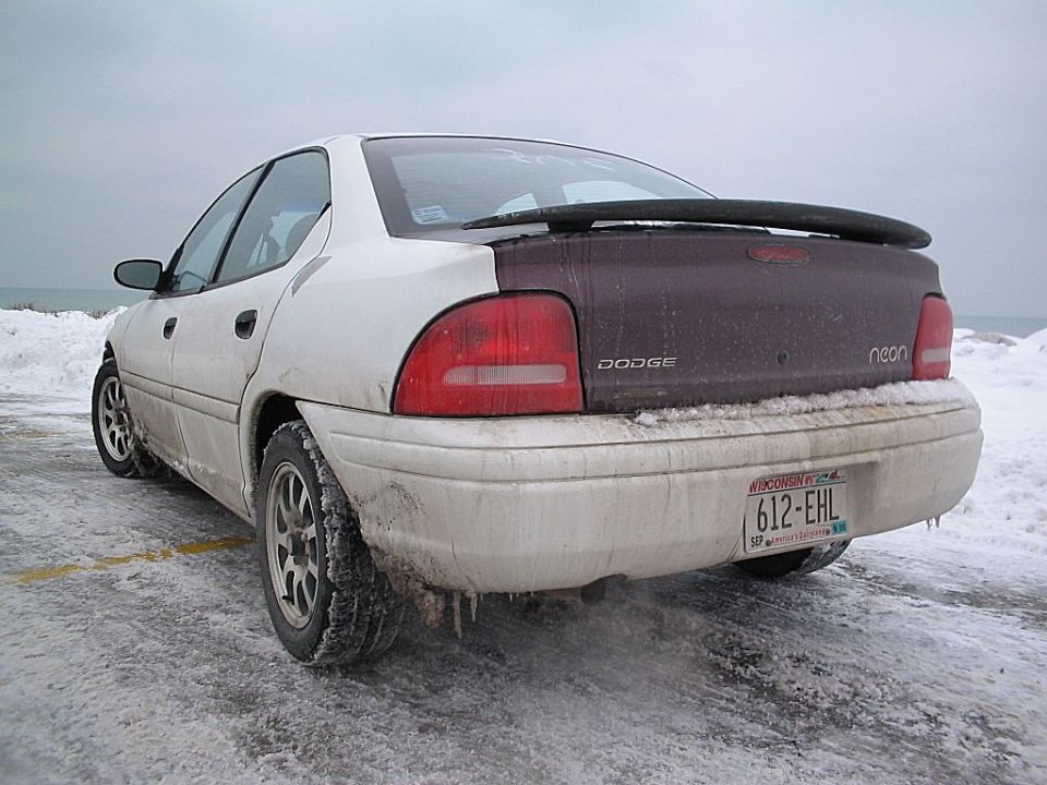 Rear view of a white and dark purple 1995 Plymouth Neon sedan with a spoiler in the snow