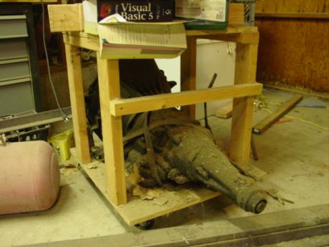 1978 Ford Bronco - A dusty transmission is supported by a wooden cart in a garage setting.