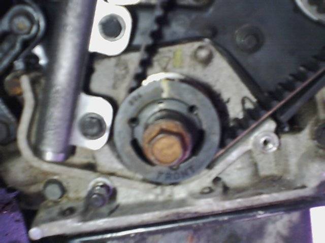 Close-up of engine timing belt, gears, and tensioner pulley with 'FRONT' marking