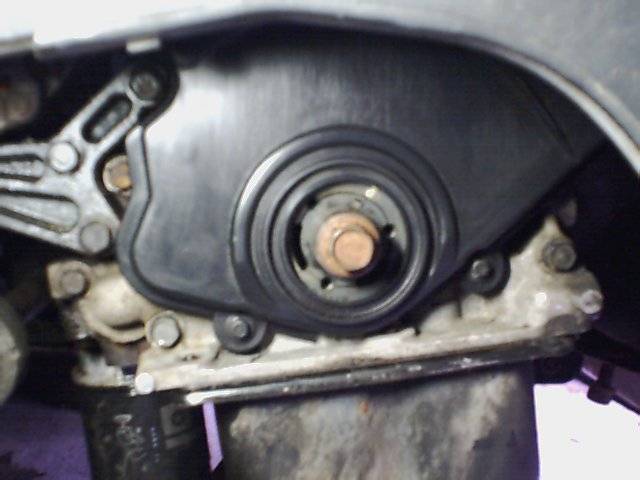 Engine timing belt cover and pulley assembly with visible bolts and a rusty bolt head
