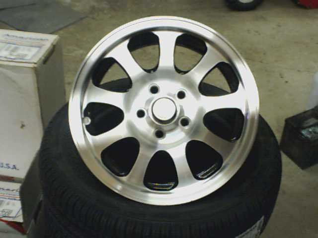 Aftermarket aluminum wheel with 5 split spokes, mounted on a tire. A cardboard box is visible to the left