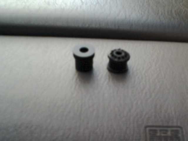 Two small black rubber parts on a metallic surface, one with a hole, the other with a ribbed pattern