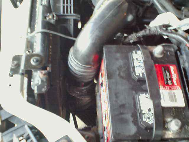 Engine bay with battery and hose. Text on battery is visible