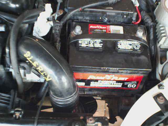 Car engine bay with a black intake hose marked with yellow text and a red and black battery