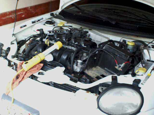 White car engine bay with a yellow work light resting on a rag over the engine components