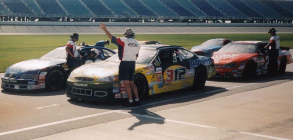 Race cars lined up on the track, one with a person waving. The car in front has 'TAURUS' on it and number 312