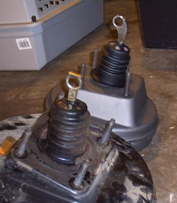 1991 Ford LTD Crown Victoria - Two vacuum brake boosters sitting on a garage floor side by side for comparison, a cleaner grey-painted unit behind and a grimier, oil-stai…